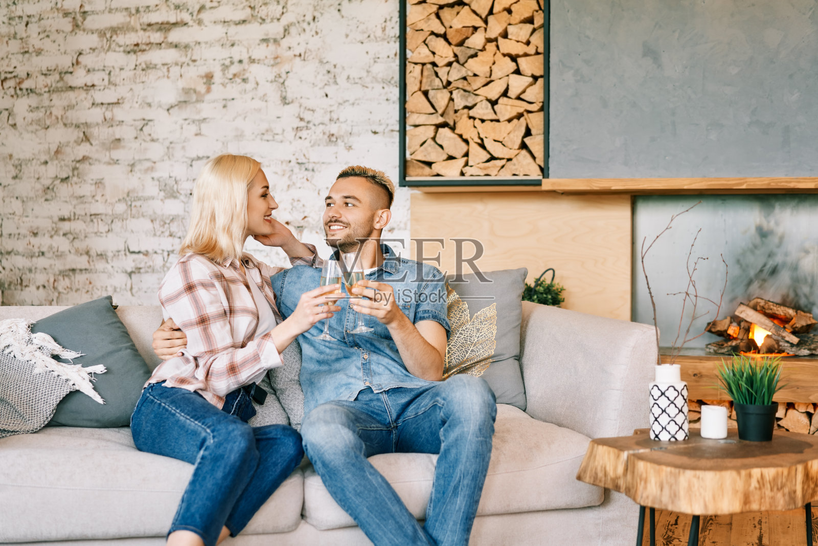 年轻幸福的夫妇喝着香槟，微笑着坐在他们现代的家里的沙发上照片摄影图片