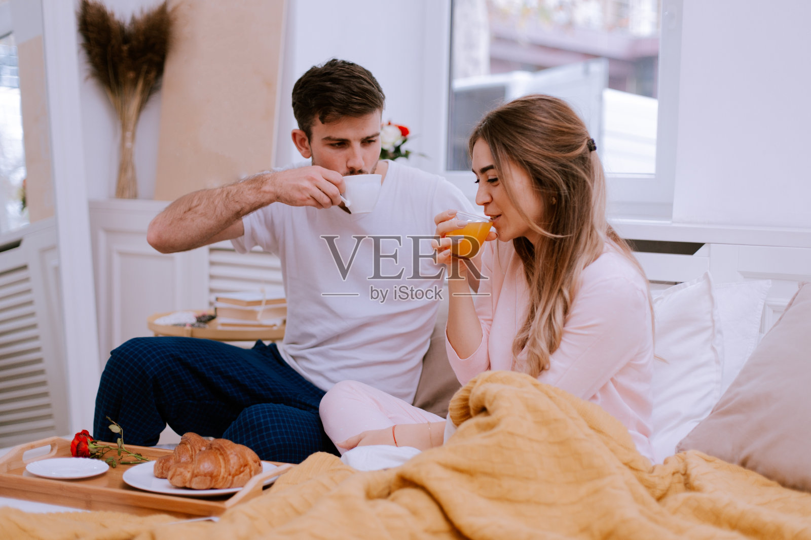 一对情侣坐在床上，供应咖啡和橙汁照片摄影图片