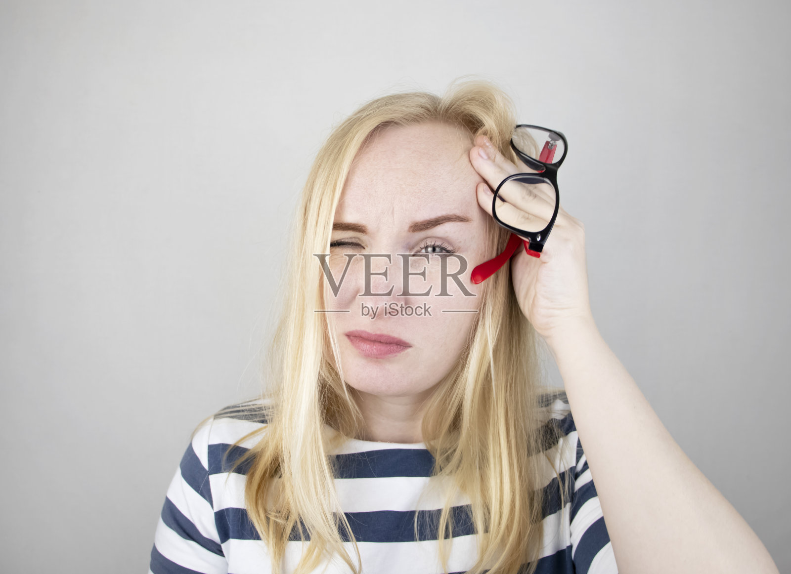 一个女人用他疲惫的双手在白色的背景上揉揉他的眼睛。来自电脑和工作的眼睛疲劳的概念。眼睛和前额疼痛，偏头痛，眼疾照片摄影图片