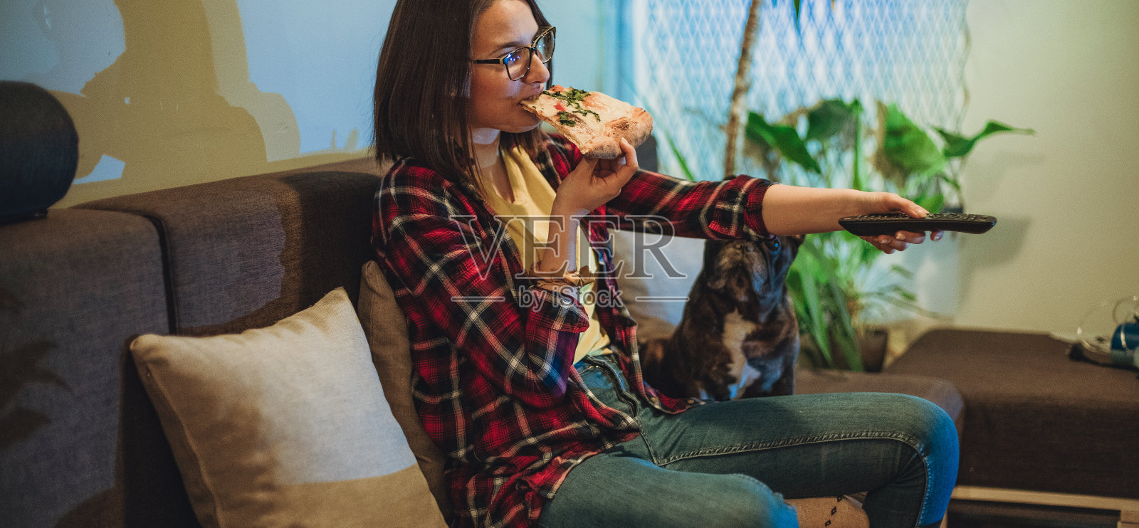一个女人在沙发上吃披萨，和她的狗一起看电视照片摄影图片