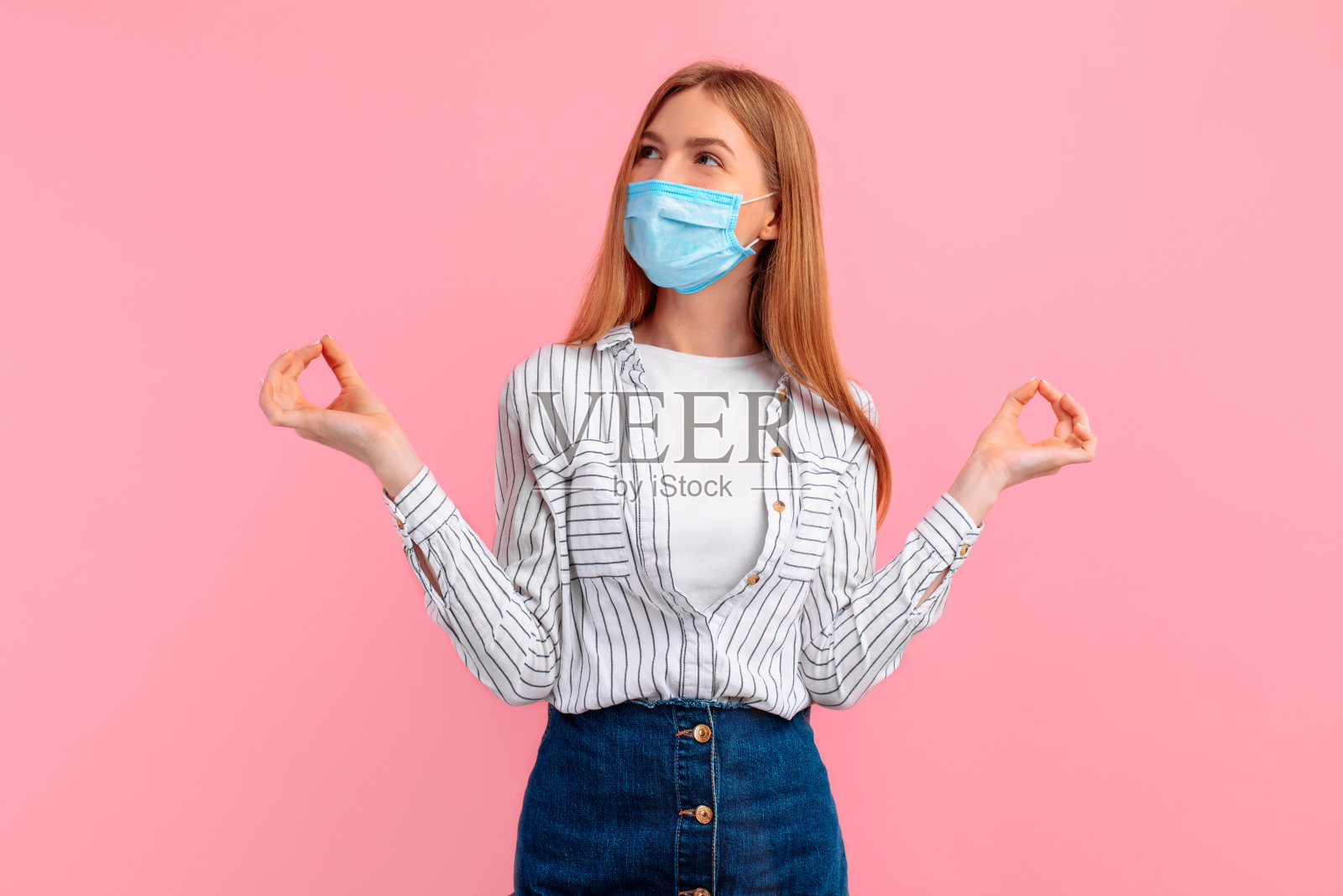 美丽的年轻女子在她的脸上一个医疗面具，站在一个瑜伽姿势和沉思孤立在一个粉红色的背景。照片摄影图片