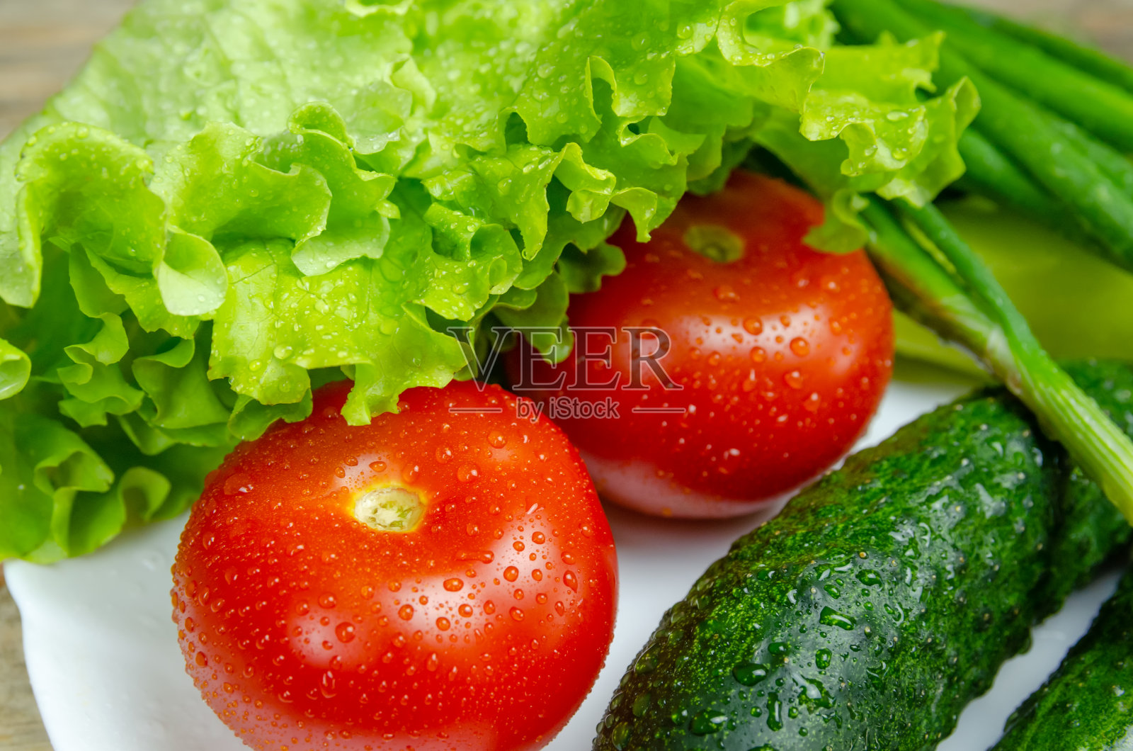 白色的盘子上放着漂亮的新鲜多汁的蔬菜，上面滴着水:新鲜的辣椒，西红柿，黄瓜，生菜，莳萝，葱照片摄影图片