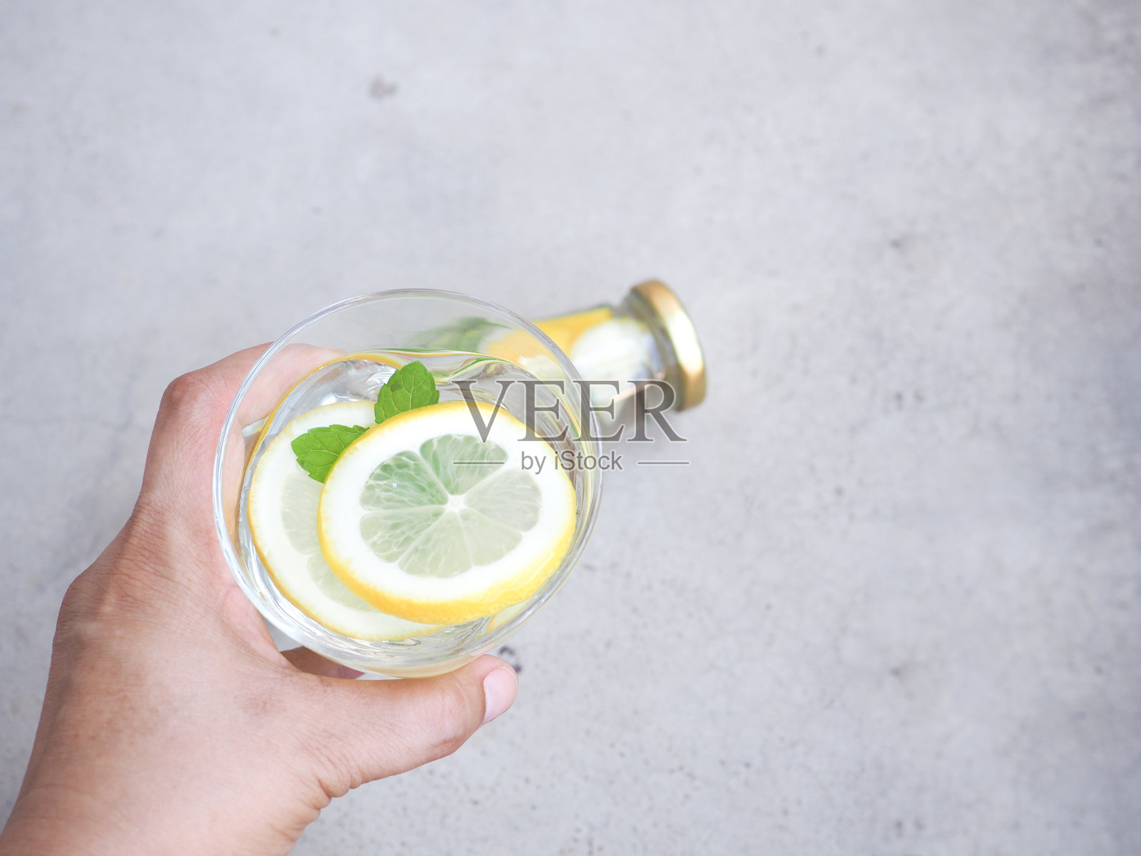 手里拿着一杯水和柠檬片和薄荷叶在灰色的背景。为文本复制空间。高维生素C。照片摄影图片