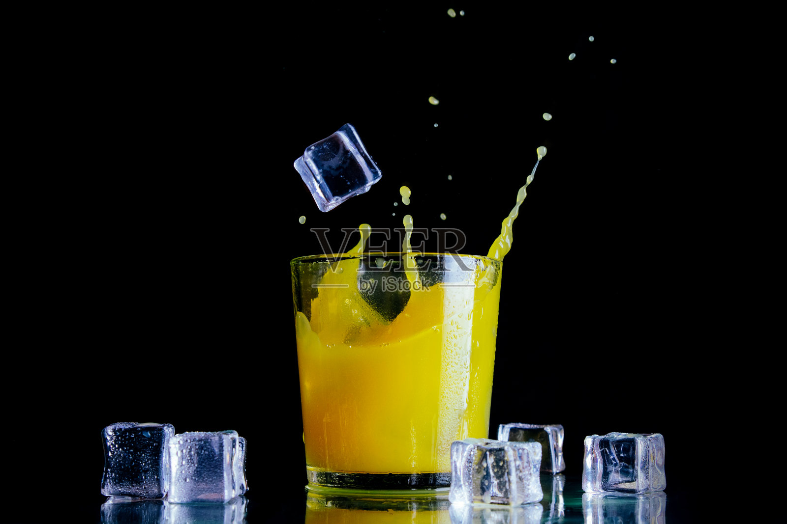 在一个透明的玻璃杯中洒上橙汁和冰块，背景是黑色的照片摄影图片