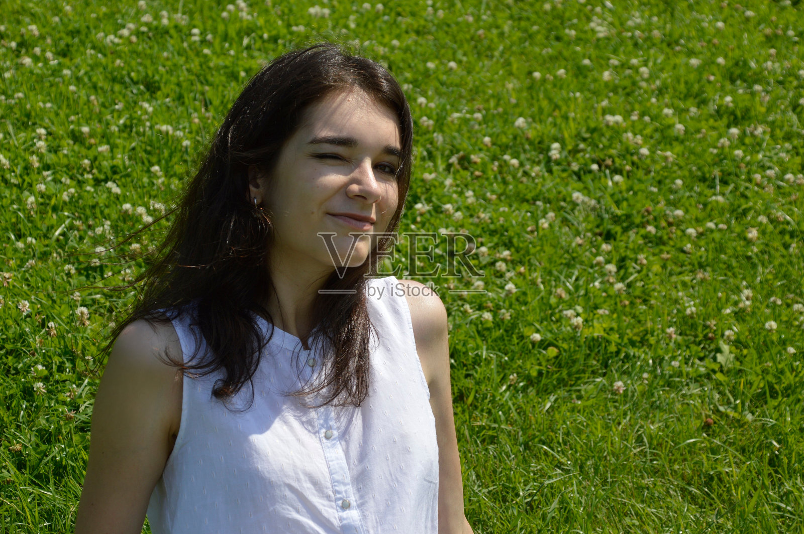 年轻的褐发女人的肖像，眨着眼睛，看着相机上的背景与三叶草绿色草地照片摄影图片