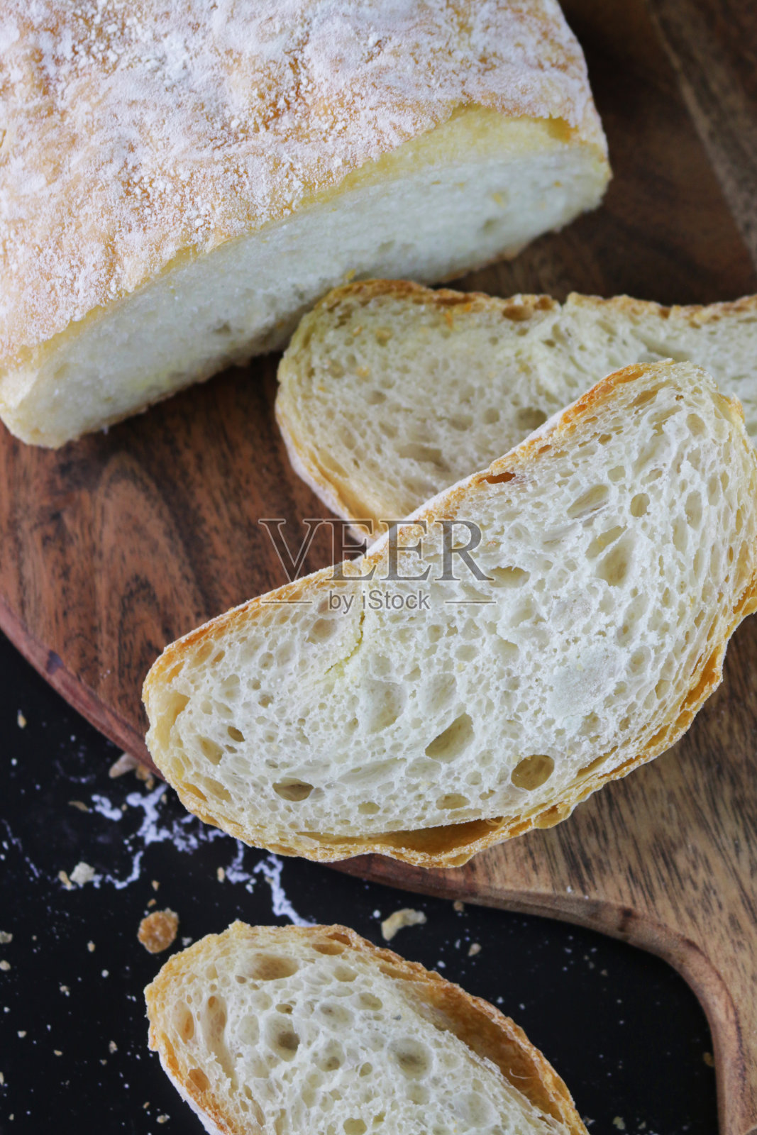 自制的查巴塔面包放在圆形的木砧板上，金黄色，刚出炉的面包，硬壳的面包切成片，高处的景色照片摄影图片