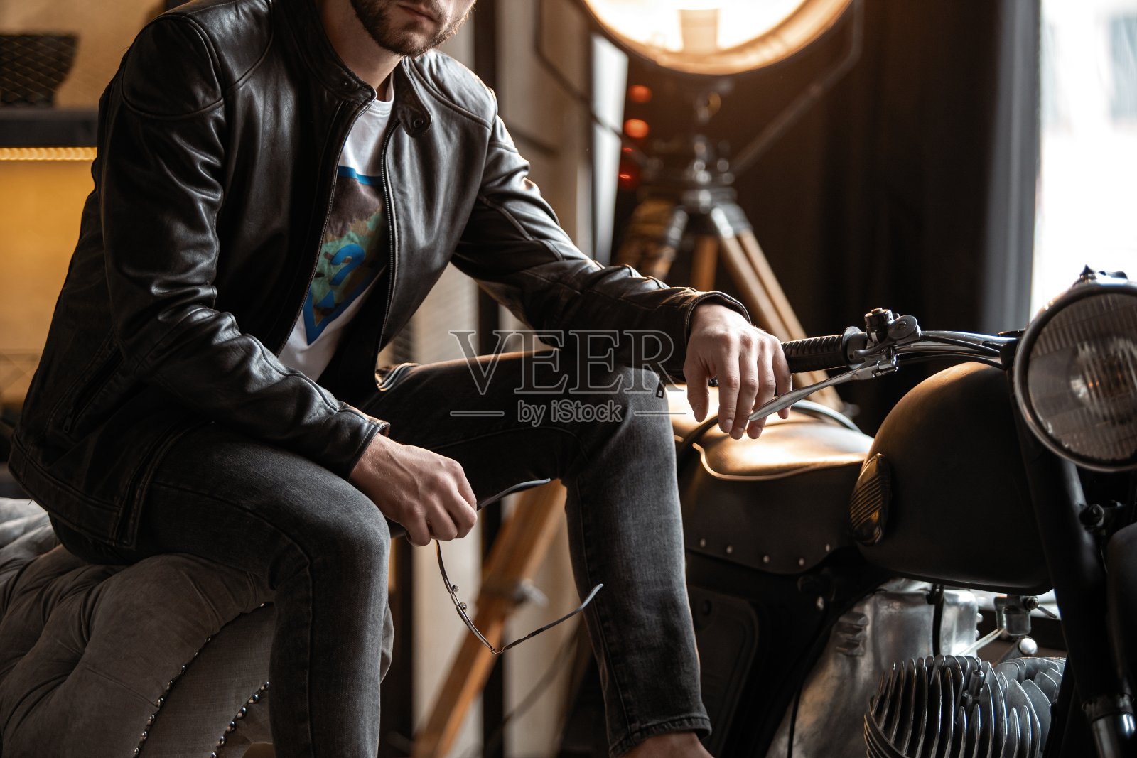 穿着皮夹克的英俊年轻人坐在凳子上看别处照片摄影图片