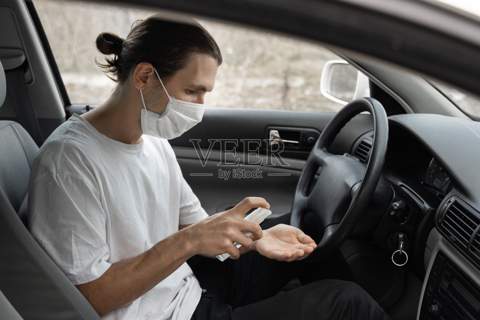 戴着医用防护口罩的人在计划开车时使用杀菌剂来保护自己免受细菌和病毒的伤害。隔离时戴口罩、大流行、新冠病毒、冠状病毒、感染。照片摄影图片