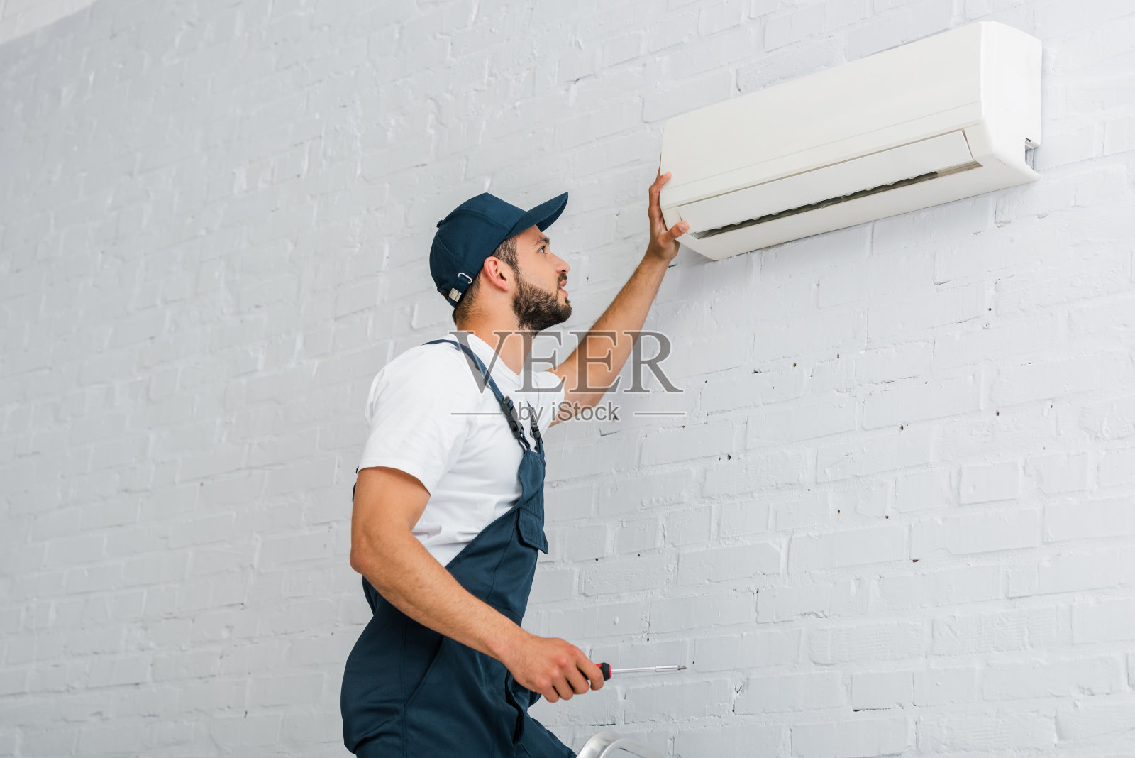 手持螺丝刀的工人侧视图，靠近空调照片摄影图片