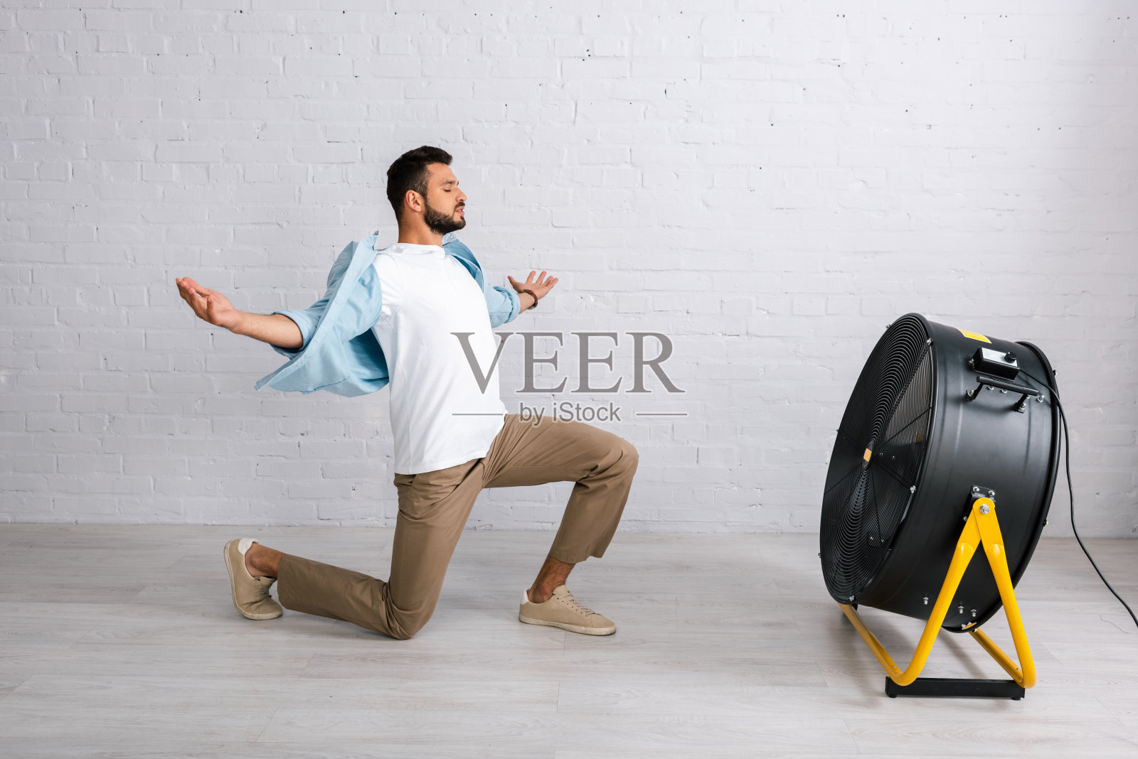 帅哥站在家里地板上电扇旁边的膝盖上照片摄影图片