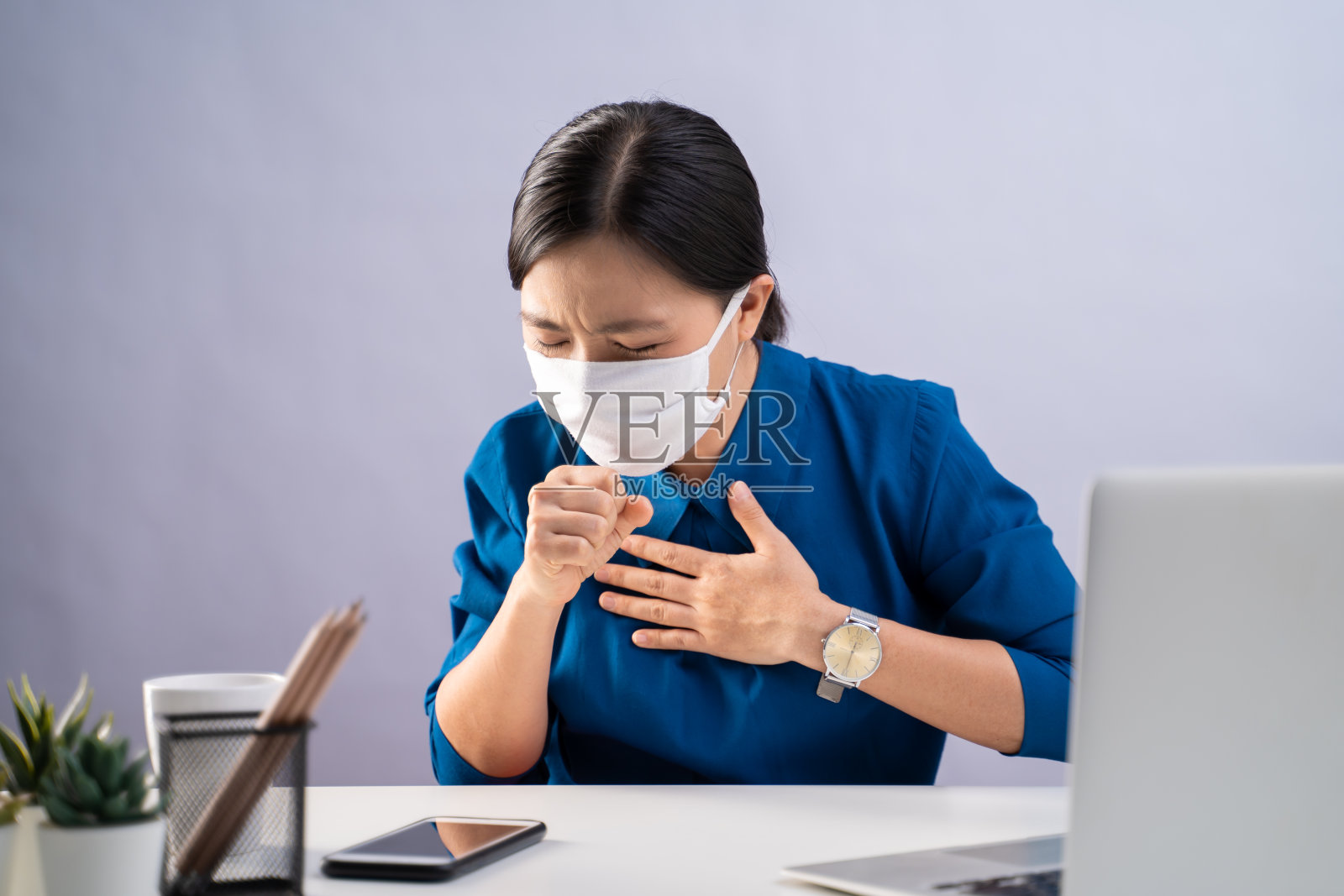 一名亚洲妇女穿着蓝色衬衫，戴着防护口罩，喉咙痛，在办公室。孤立在白色背景上。照片摄影图片