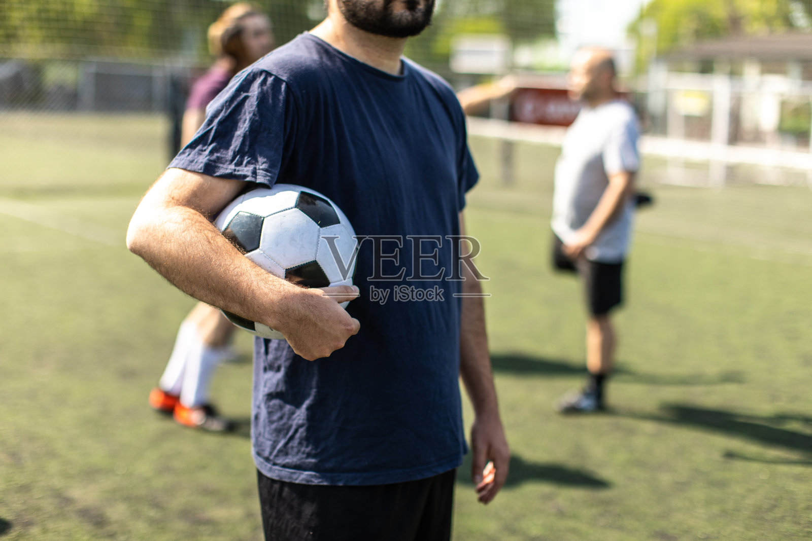 一个人站在足球场上，胳膊里抱着球照片摄影图片