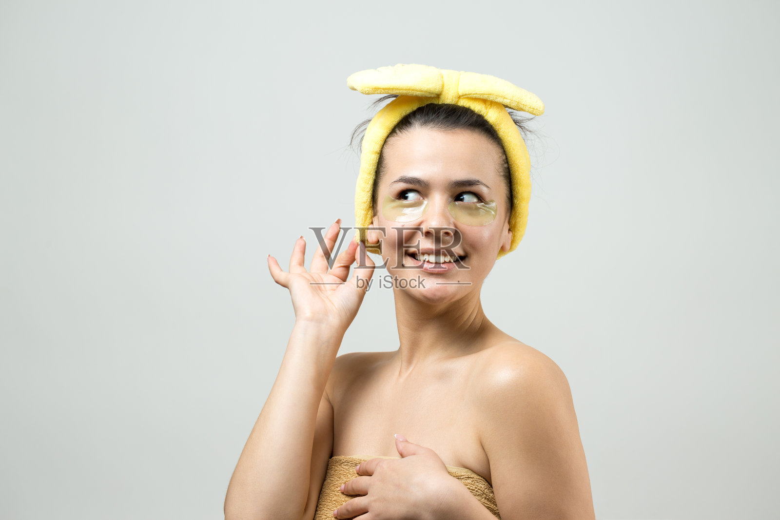 年轻美丽的女孩在一个白色的毛巾在他的头上戴着胶原凝胶眼罩。敷眼罩治疗面部。照片摄影图片