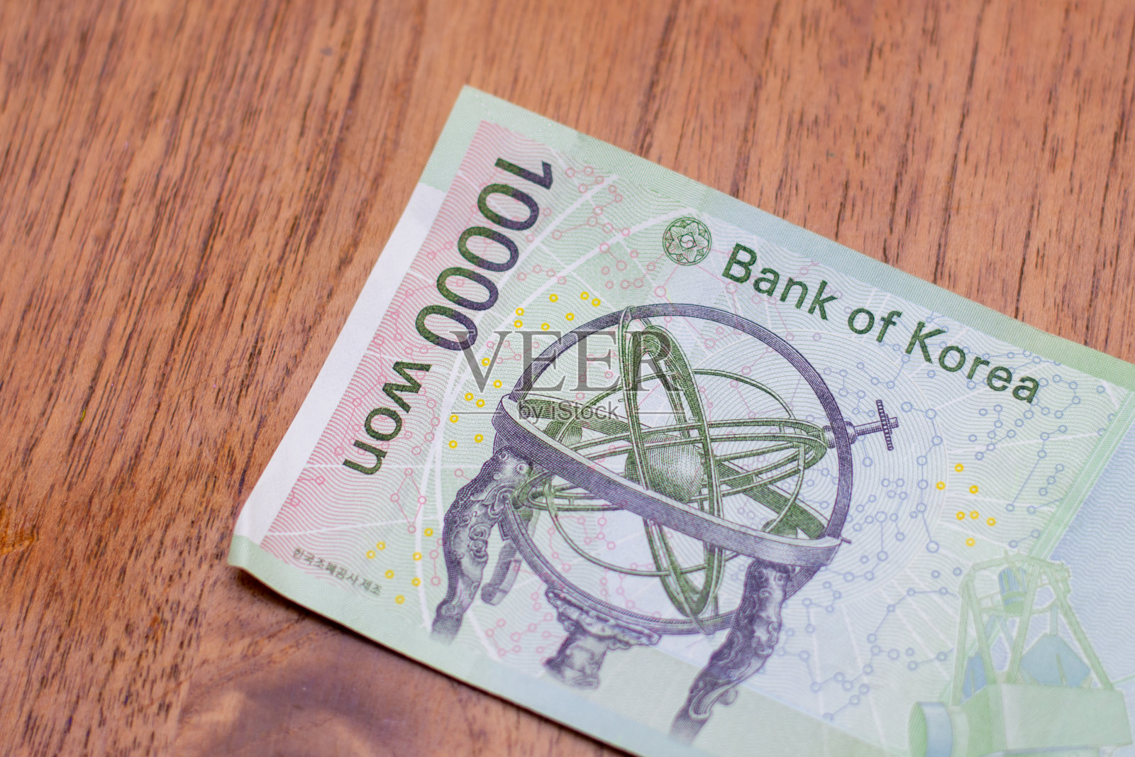 韩国的货币-接近一个绿色的一万韩元钞票在一个棕色的桌子的背景。金钱交换。照片摄影图片