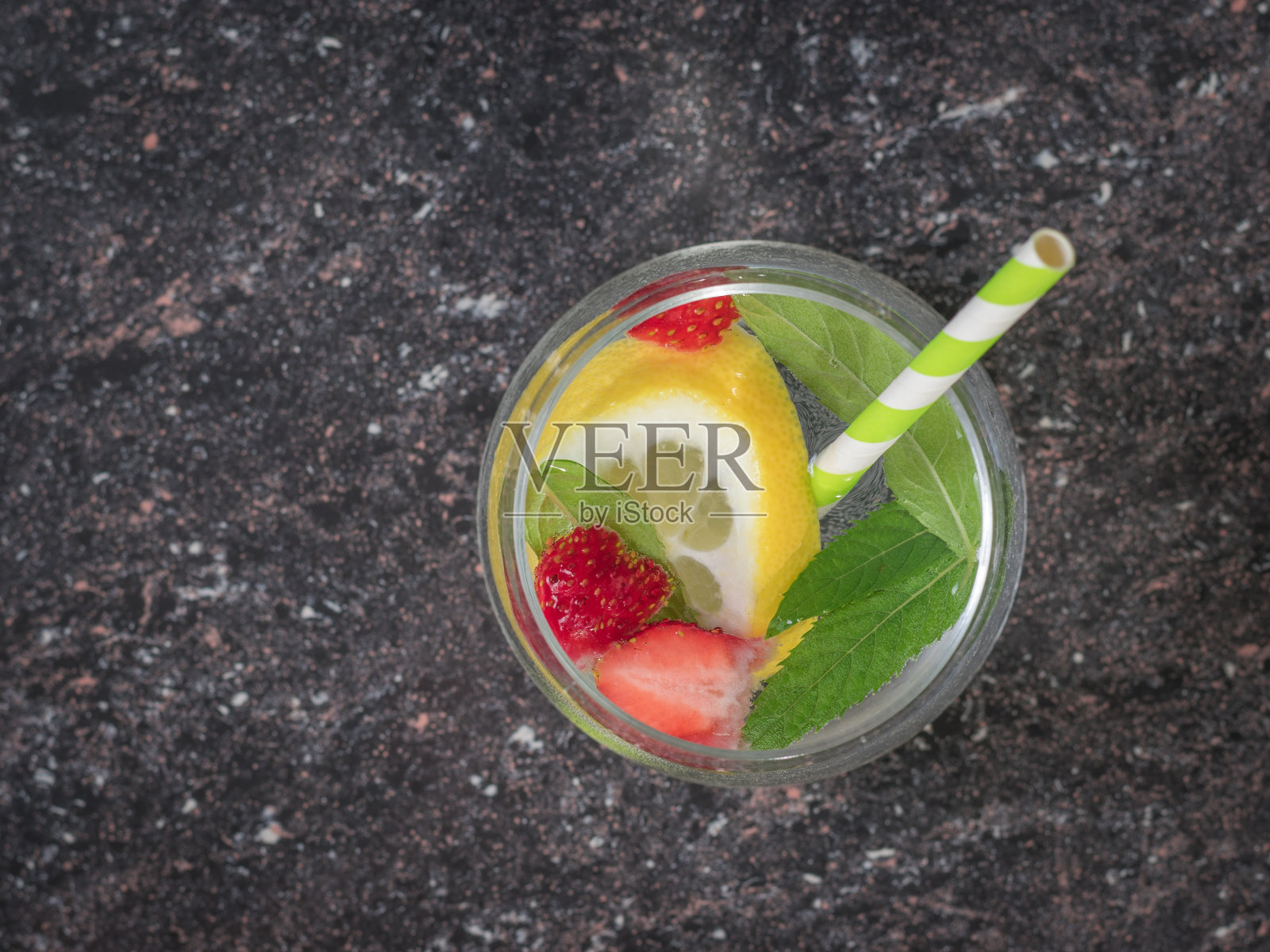 绿色鸡尾酒管在一杯冰水中加入柠檬，薄荷和浆果。照片摄影图片