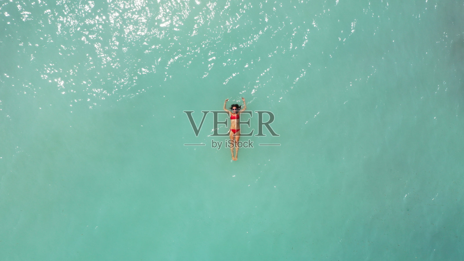 年轻美丽的女人在红色比基尼和太阳镜的鸟瞰图躺在浅蓝色蓝绿色的海水，在海洋放松。夏日海滩度假。马里布救生员。马尔代夫。Melasti海滩。印度尼西亚巴厘岛照片摄影图片