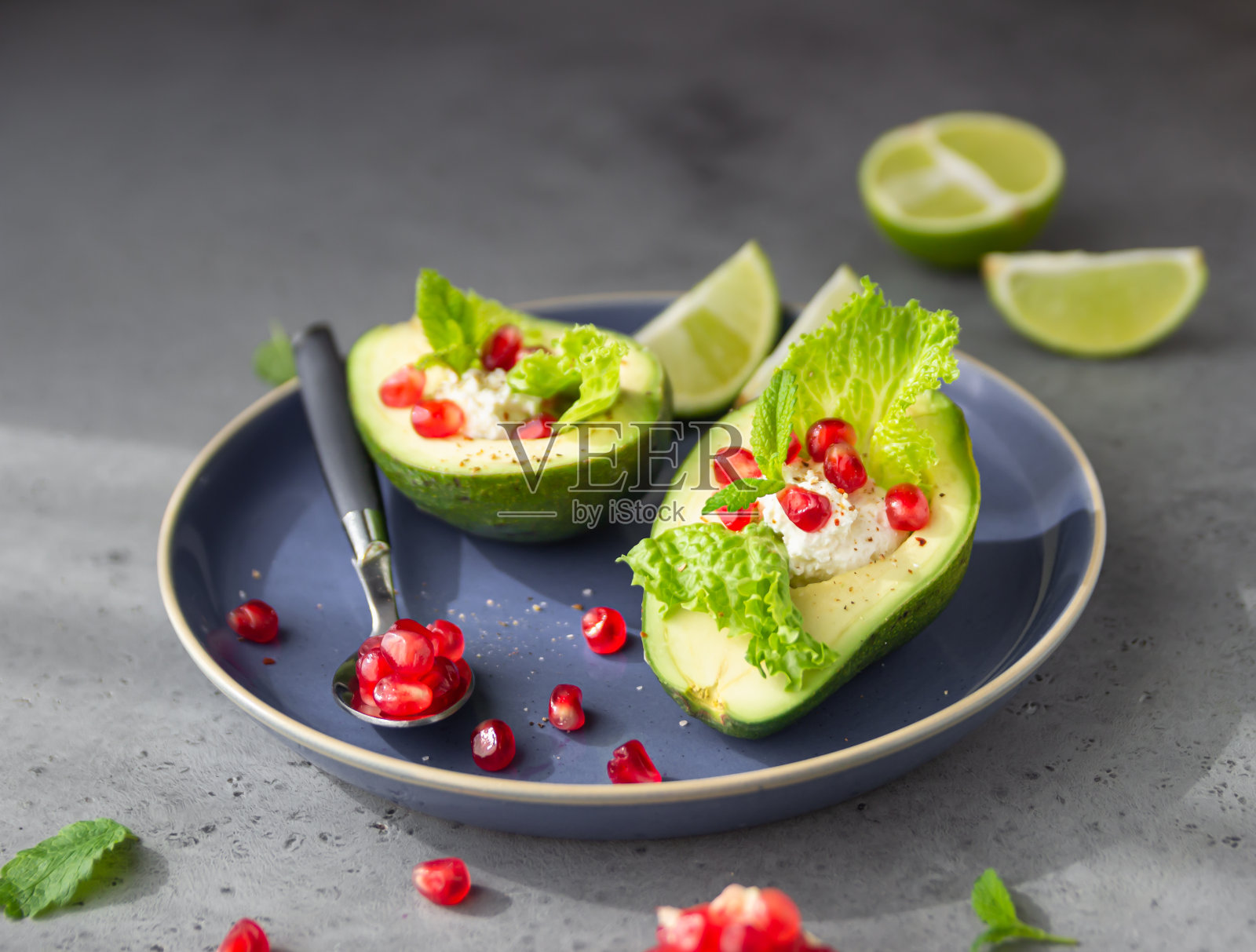 牛油果，石榴籽，乳清干酪或奶油奶酪，莴苣叶和薄荷放在蓝色陶瓷盘子里。健康的有机素食食品。照片摄影图片