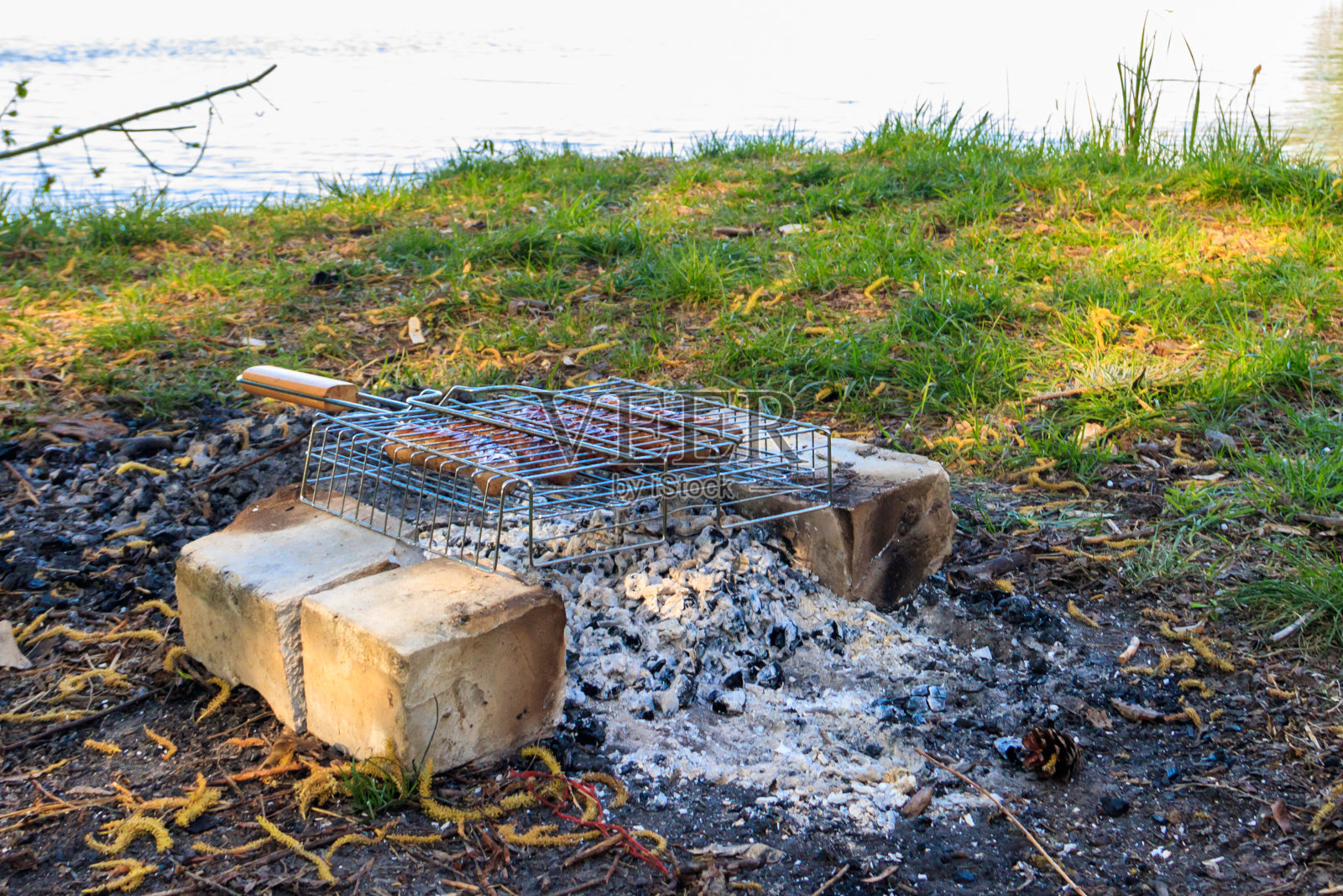 在河边的篝火上用便携式烧烤架烤香肠照片摄影图片