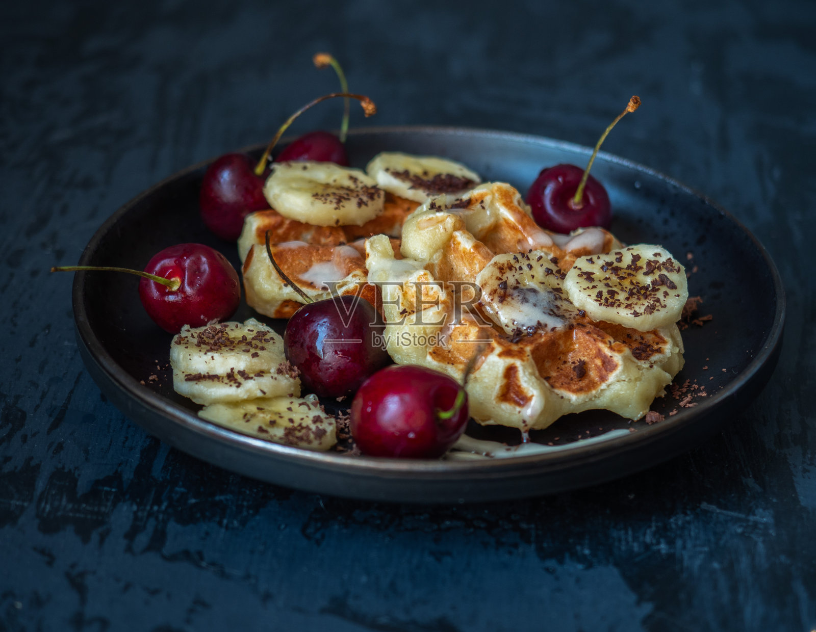 在黑色的盘子里放上自制的奶酪和香蕉华夫饼，还有香蕉、樱桃和碎巧克力照片摄影图片