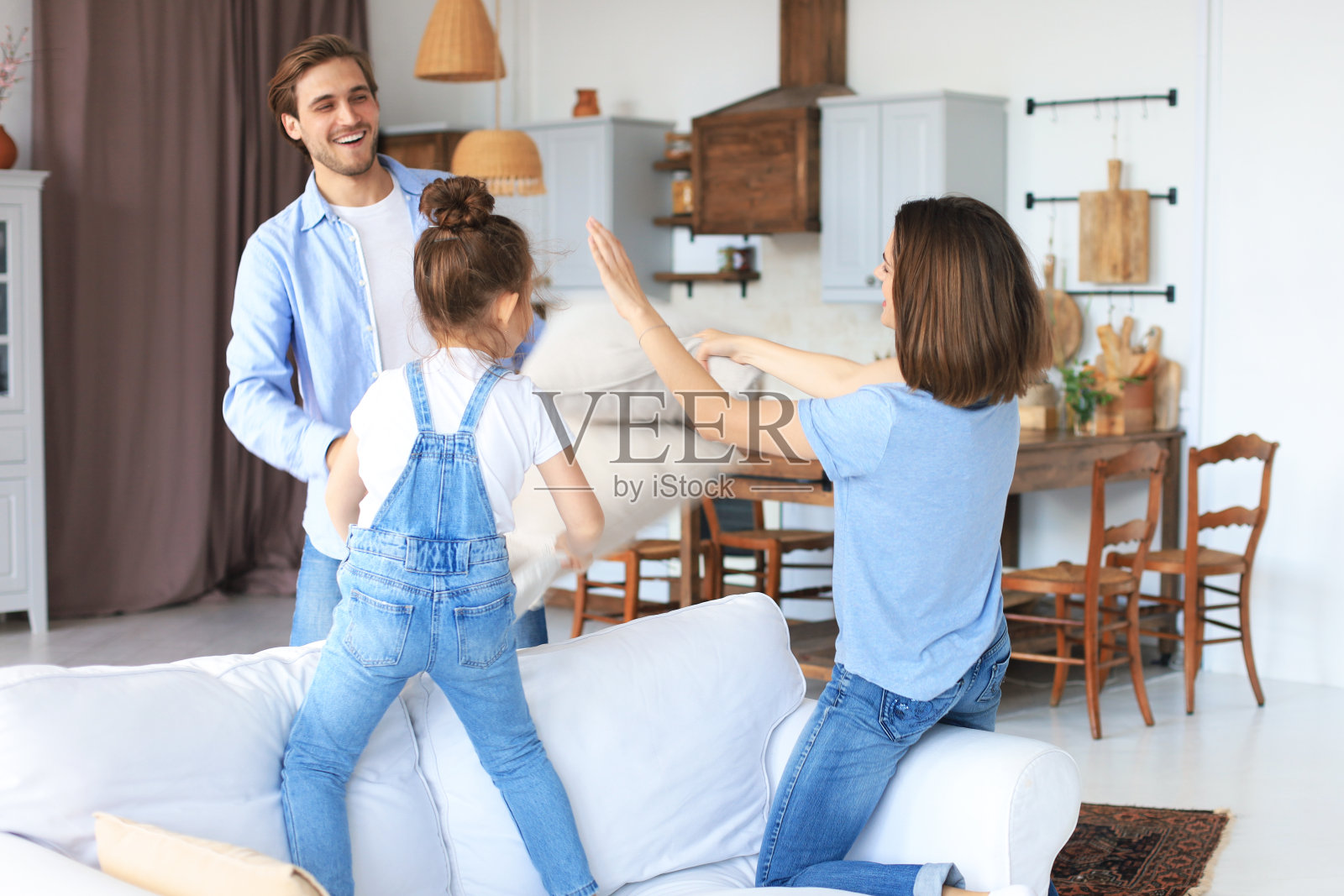 幸福的年轻家庭在沙发上玩枕头。照片摄影图片