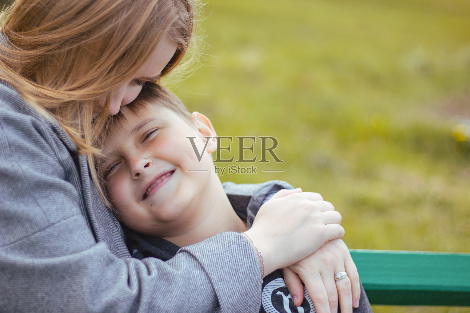 一个快乐的小男孩拥抱着他的妈妈。妈妈拥抱她的儿子。公园里的家庭照片摄影图片