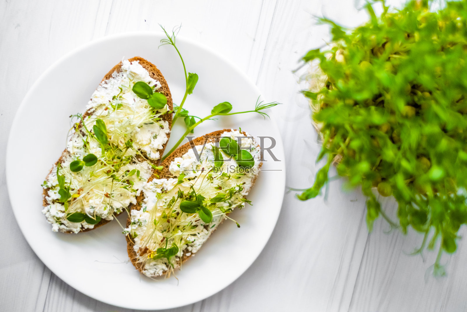 夹着白干酪和蔬菜芽的三明治放在盘子里，这是素食主义者的生活方式照片摄影图片