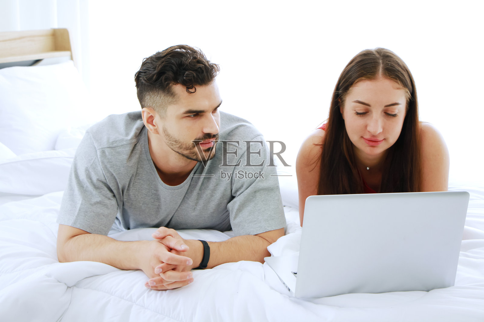 年轻的白人夫妇放松与笔记本电脑在社交媒体网上购物在卧室。技术为已婚家庭的生活方式度假概念。照片摄影图片