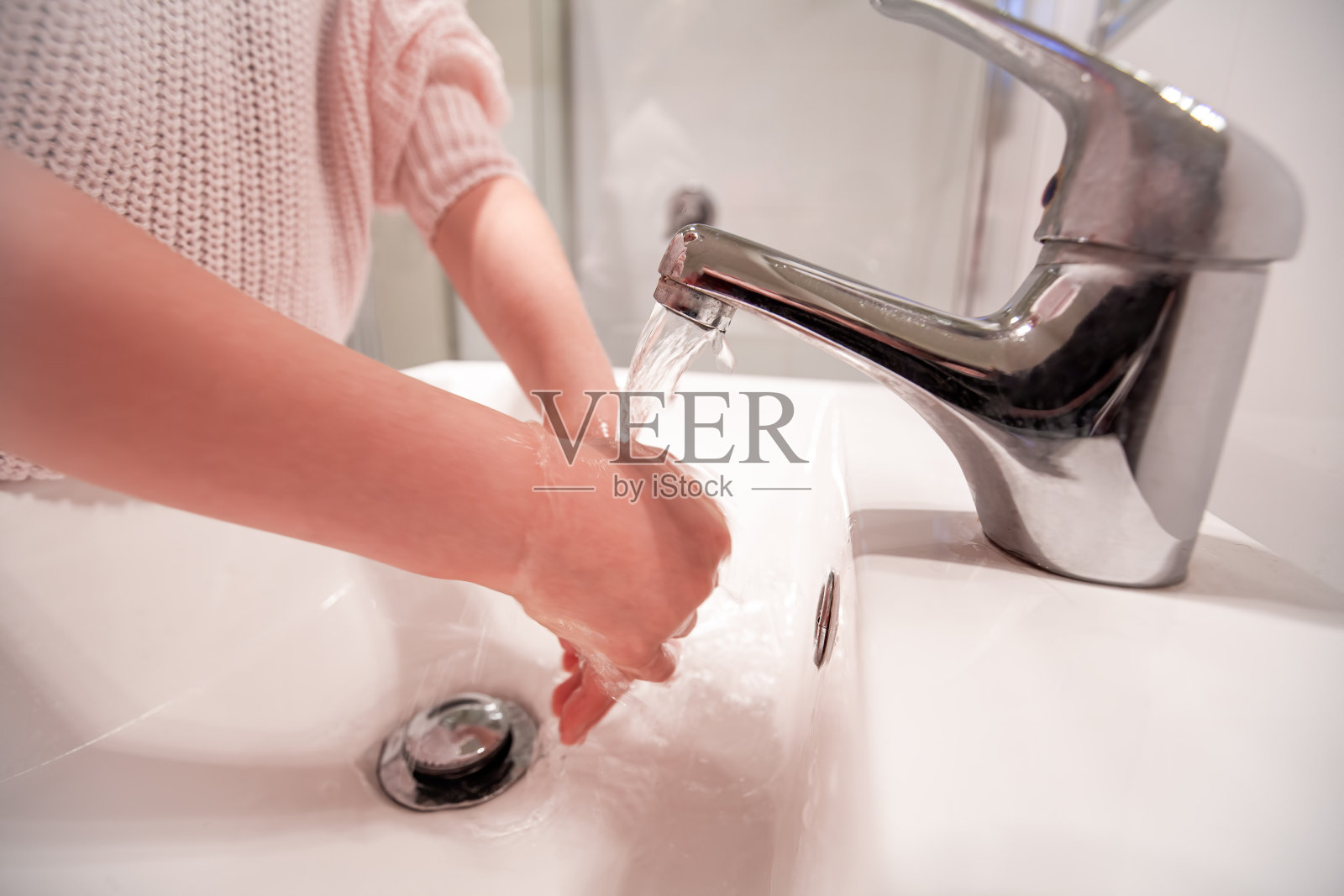 一个白人女孩在浴室水槽里的自来水下洗手照片摄影图片