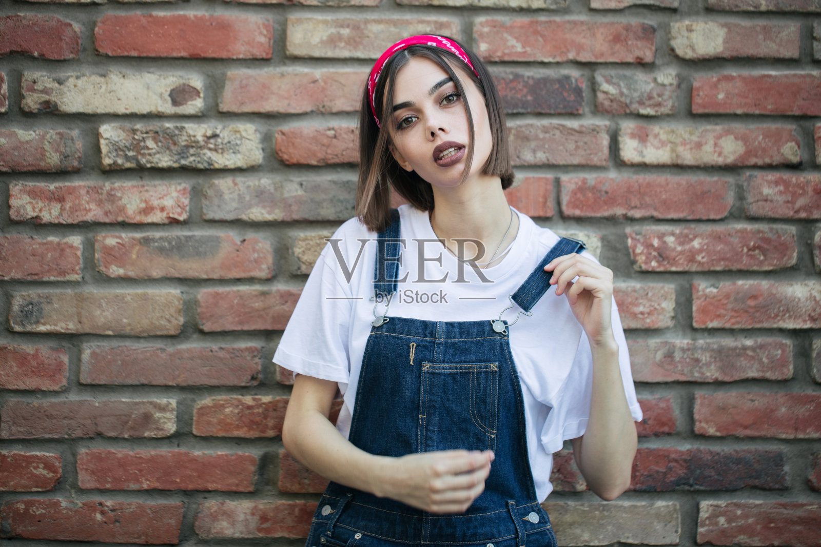 苗条性感的黑发女孩穿着女人的牛仔布整体在绿树墙纹理在城市地区照片摄影图片