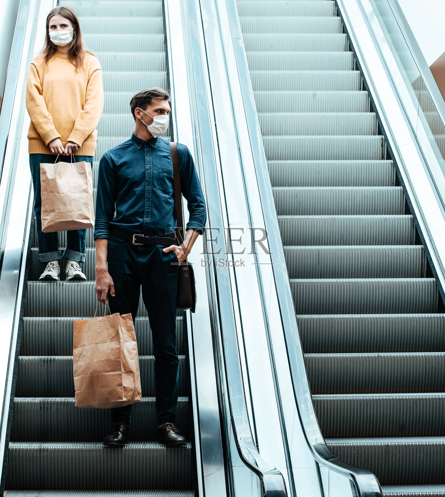 一个戴着防护面具的年轻人站在购物中心的自动扶梯上照片摄影图片