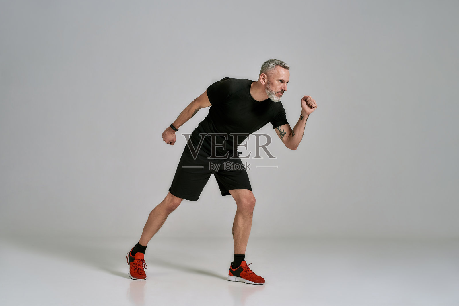 全长镜头的中年肌肉男子在黑色运动服看一边，而在工作室在灰色的背景照片摄影图片