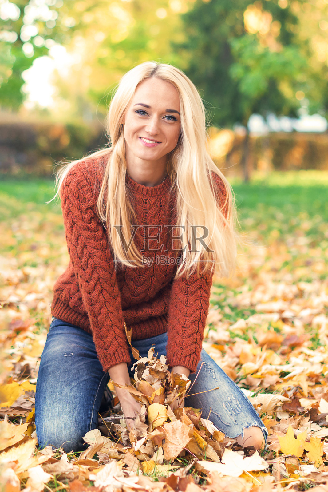 在秋天的公园里，拿着枫叶的女人照片摄影图片