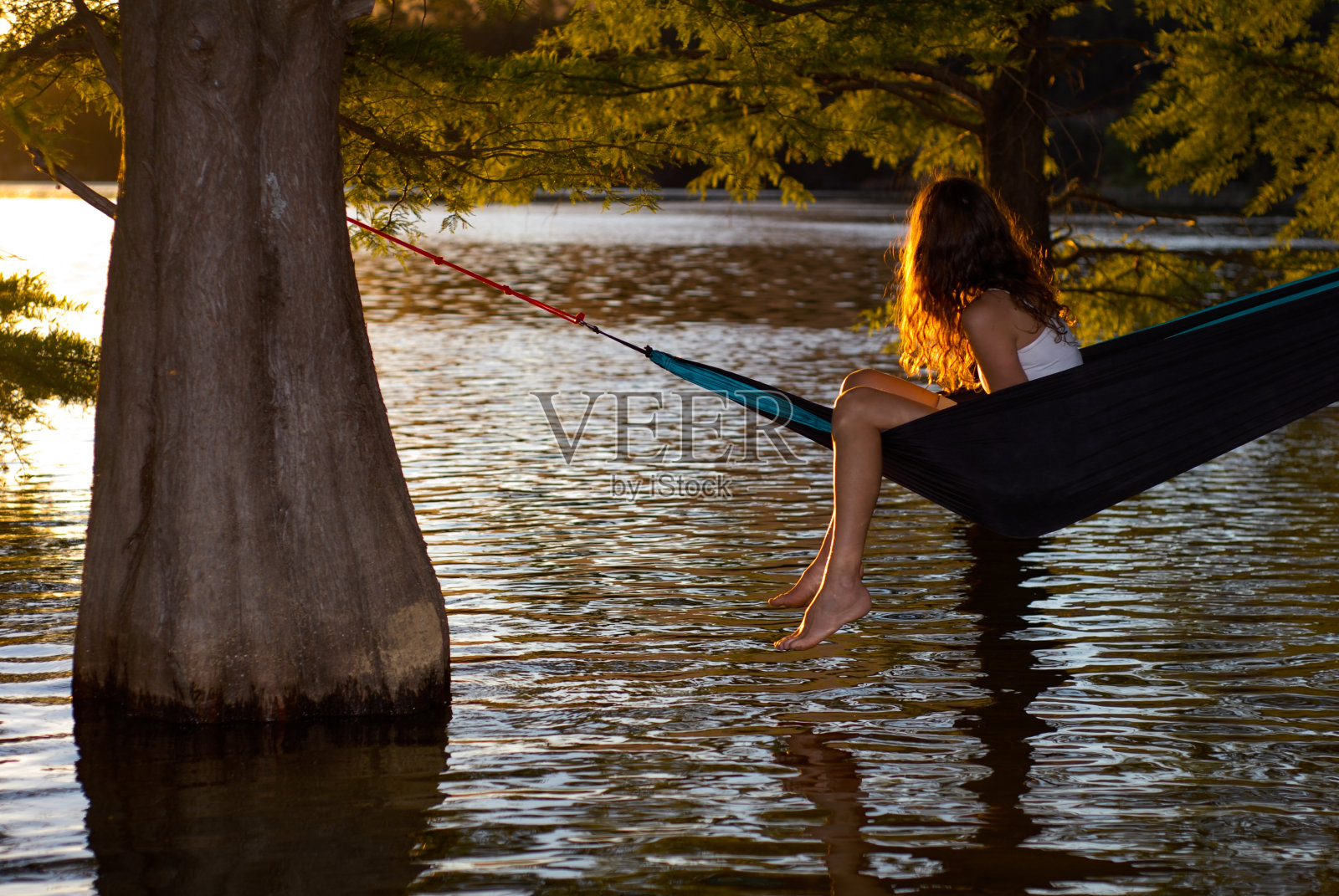 美丽的女人躺在吊床上，夕阳下，湖边的一棵树上照片摄影图片