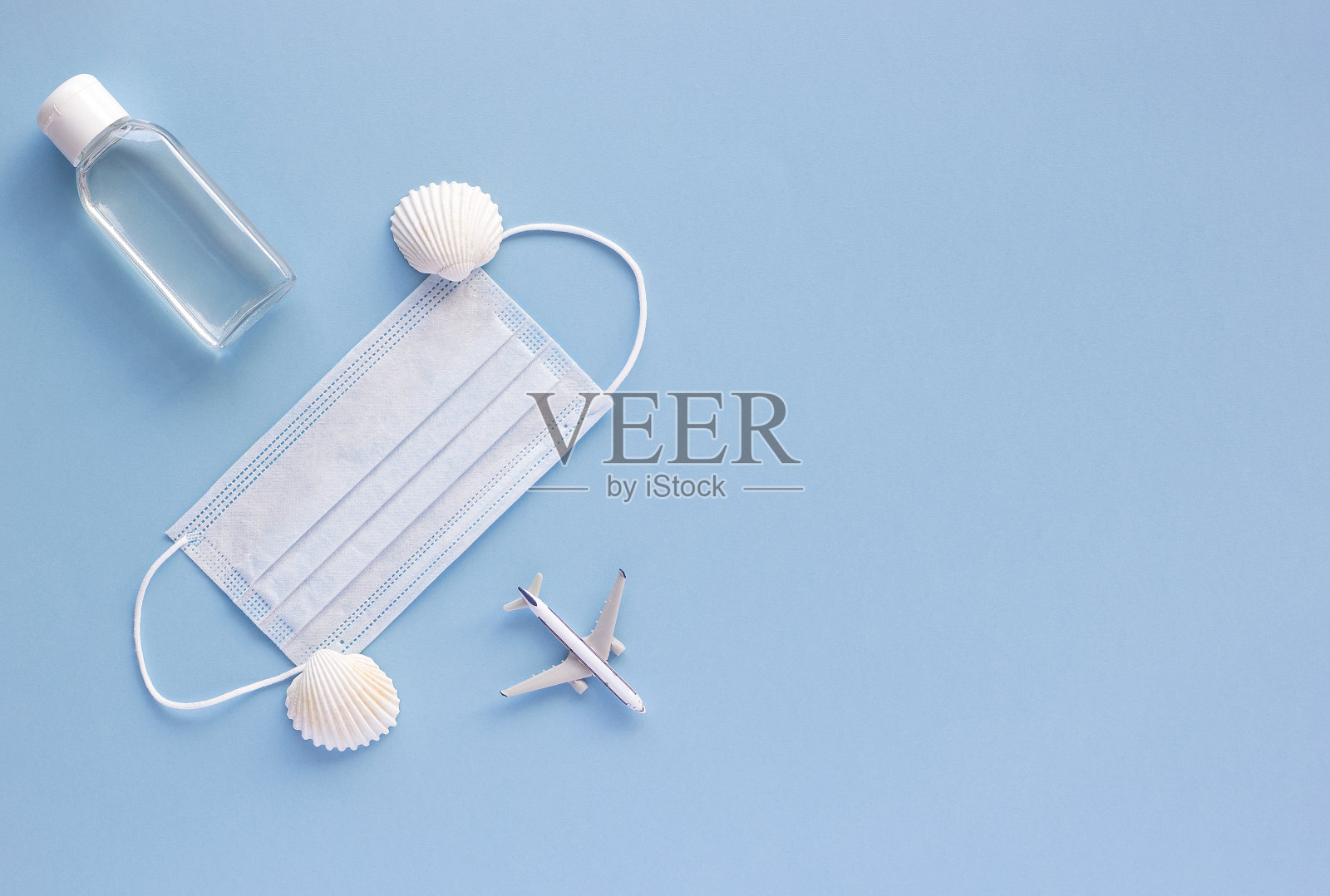 俯视图的医疗口罩，飞机模型，消毒凝胶上的蓝色背景与复制空间。在旅行期间预防冠状病毒或COVID-19的概念。平铺，拷贝空间。照片摄影图片