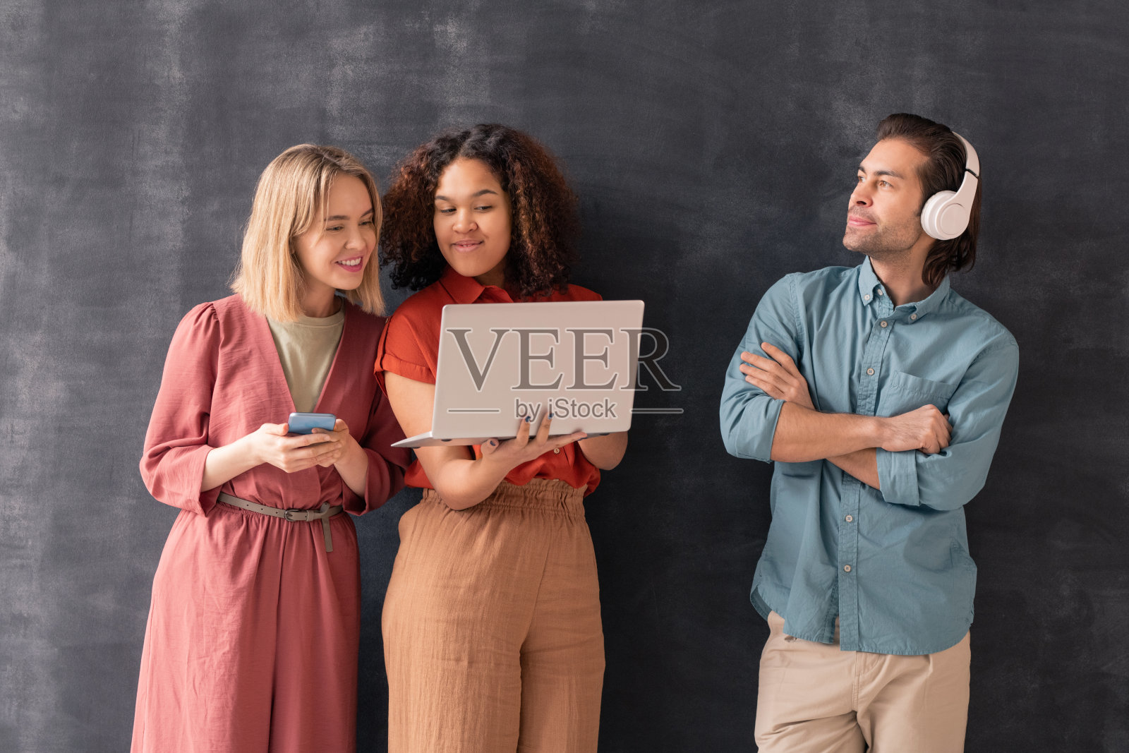 女孩拿着智能手机看她的混血儿朋友拿着的笔记本电脑照片摄影图片