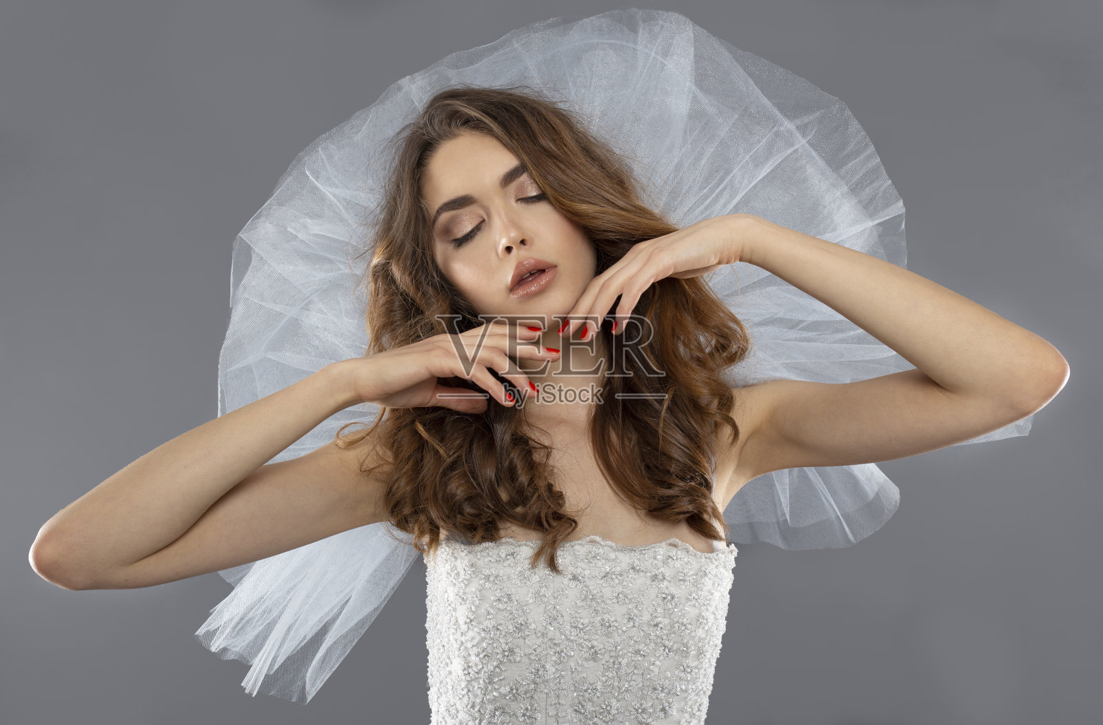 一个年轻女子的肖像在程式化的时尚婚纱，闭上眼睛，化妆，在灰色的背景。照片摄影图片