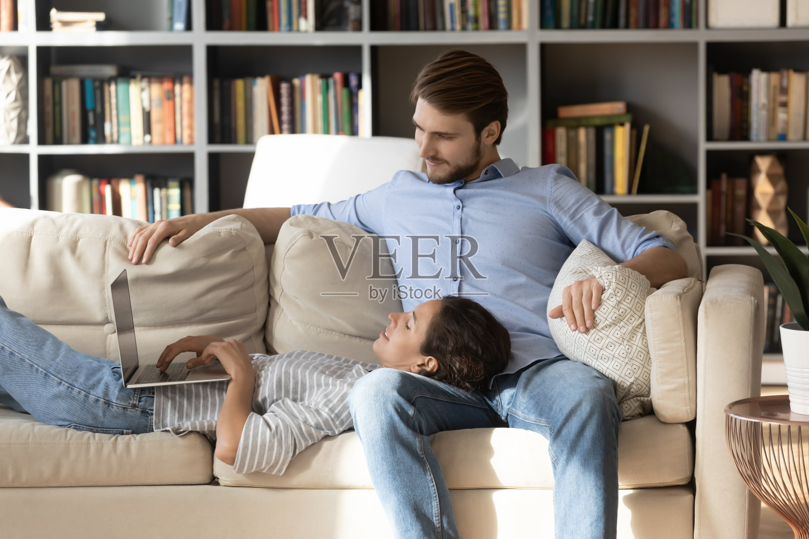 满意的年轻女子使用笔记本电脑，躺在男人腿上照片摄影图片