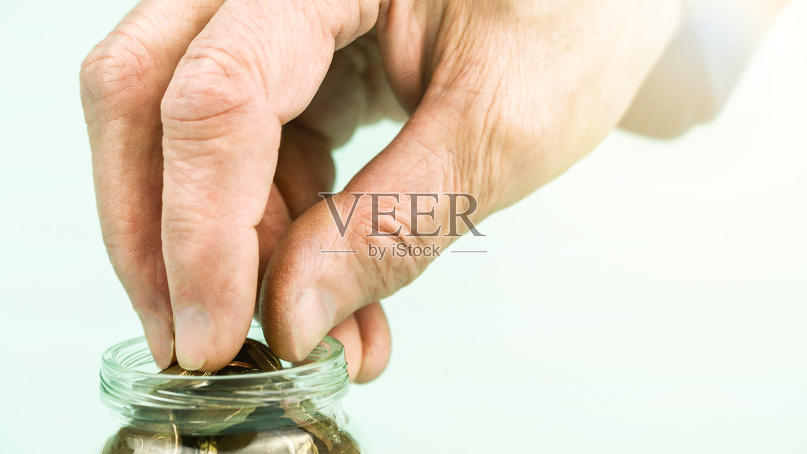 老人手从小玻璃容器中取出金币照片摄影图片