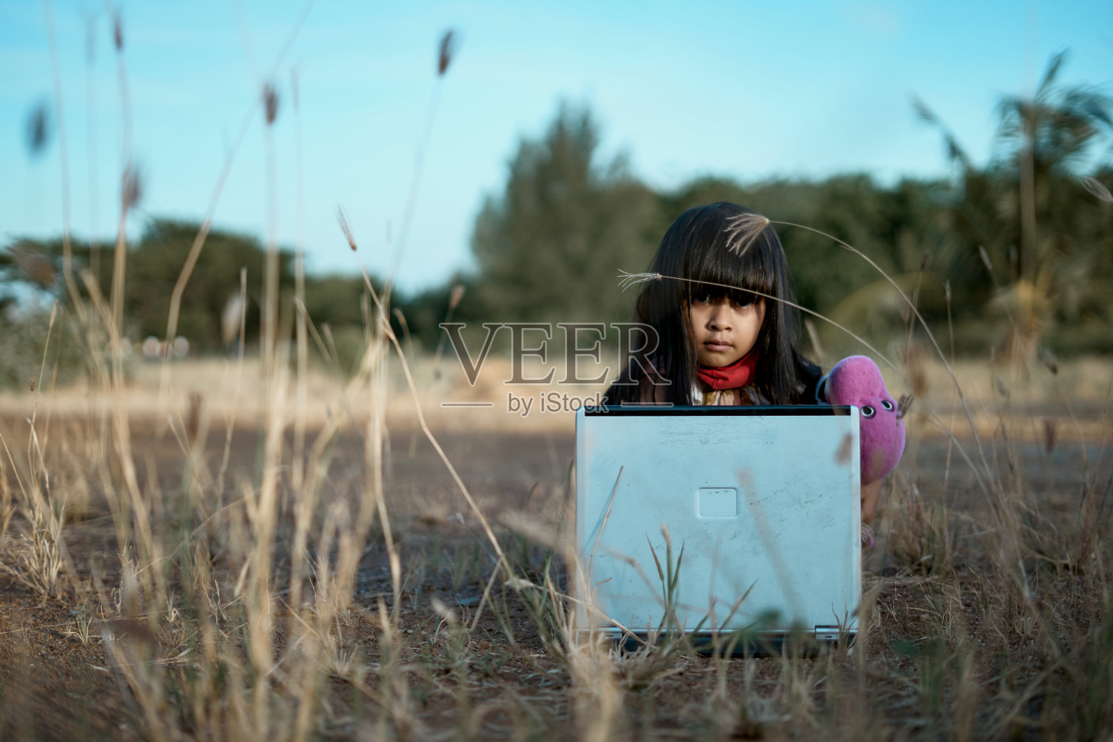 可爱的小女孩戴着保护面罩，坐在草地上使用笔记本电脑照片摄影图片