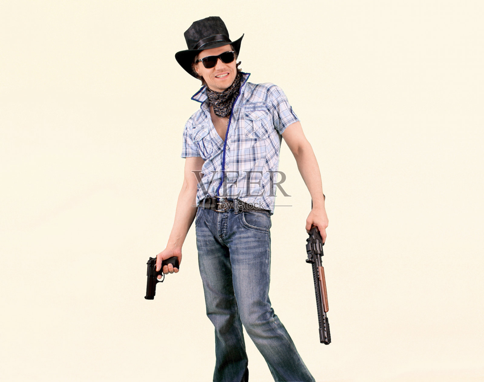 一个穿着牛仔裤，戴着墨镜，手拿手枪和来福枪的酷酷的年轻人，在白色的背景下向前看着，放肆地微笑着。照片摄影图片