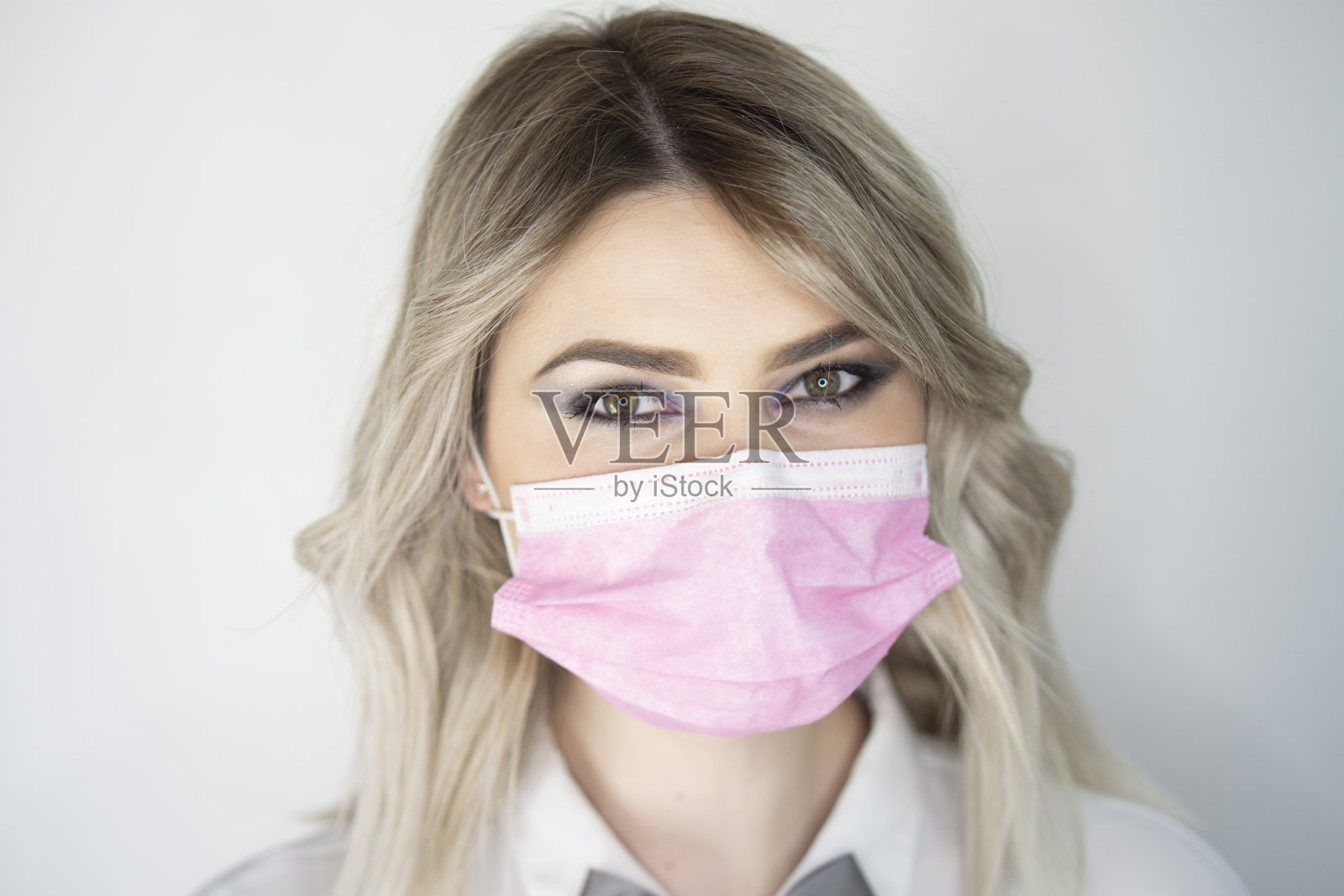 漂亮的金发女郎戴上了粉色防护面具照片摄影图片