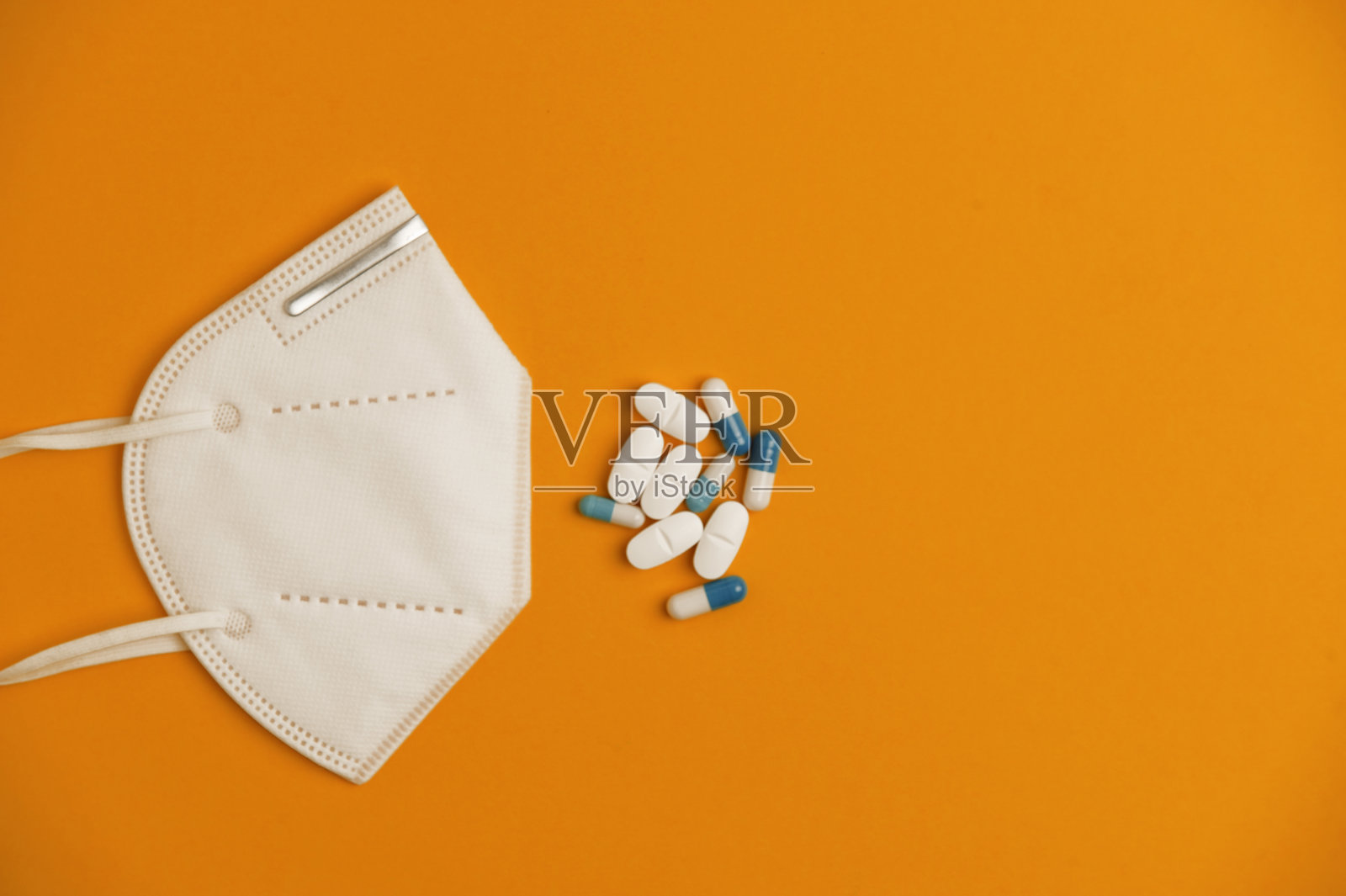 Covid-19概念:白色nk95口罩，白色和蓝色药丸组，橙色背景。俯视图照片摄影图片