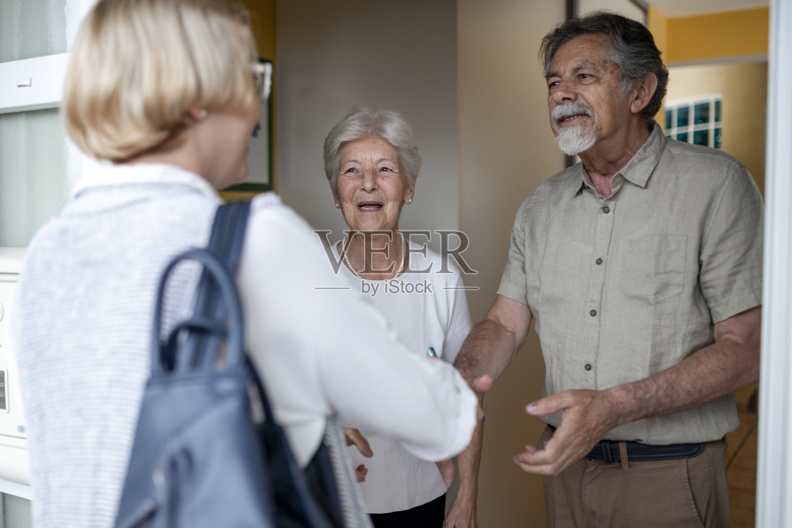 一对老年夫妇打开前门，迎接一名女性保健工作者进行家庭健康访问照片摄影图片
