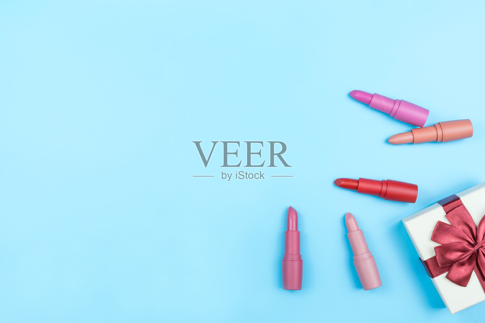 裸色口红排列在蓝色背景与红色丝带绑礼盒，复制空间照片摄影图片