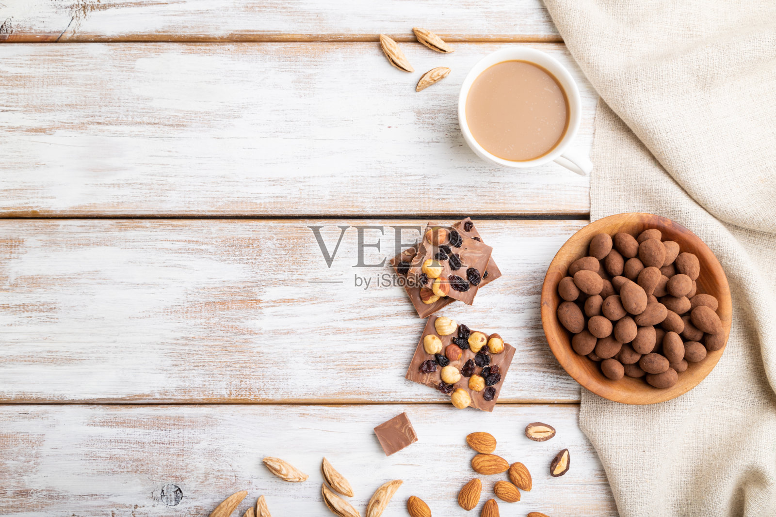 杏仁在巧克力糖霜木盘子和一杯咖啡在白色的木制背景和亚麻纺织品。俯视图，复制空间，平放。照片摄影图片