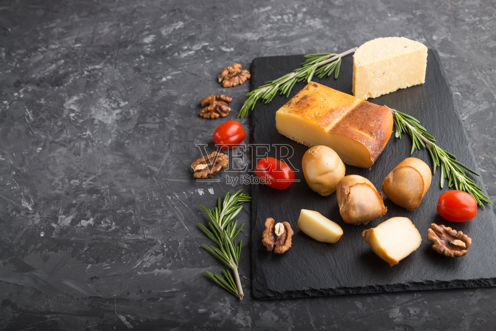 熏奶酪和各种类型的奶酪与迷迭香和西红柿在黑色的石板在黑色的混凝土背景。侧视图，拷贝空间，选择性焦点。照片摄影图片