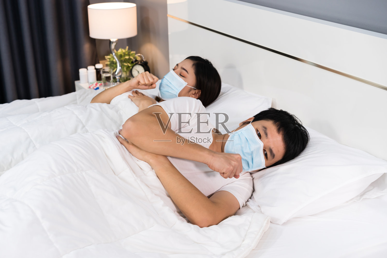 戴医用口罩的患病夫妇咳嗽、患有病毒性疾病和发热卧床，冠状病毒(covid-19)大流行概念。照片摄影图片