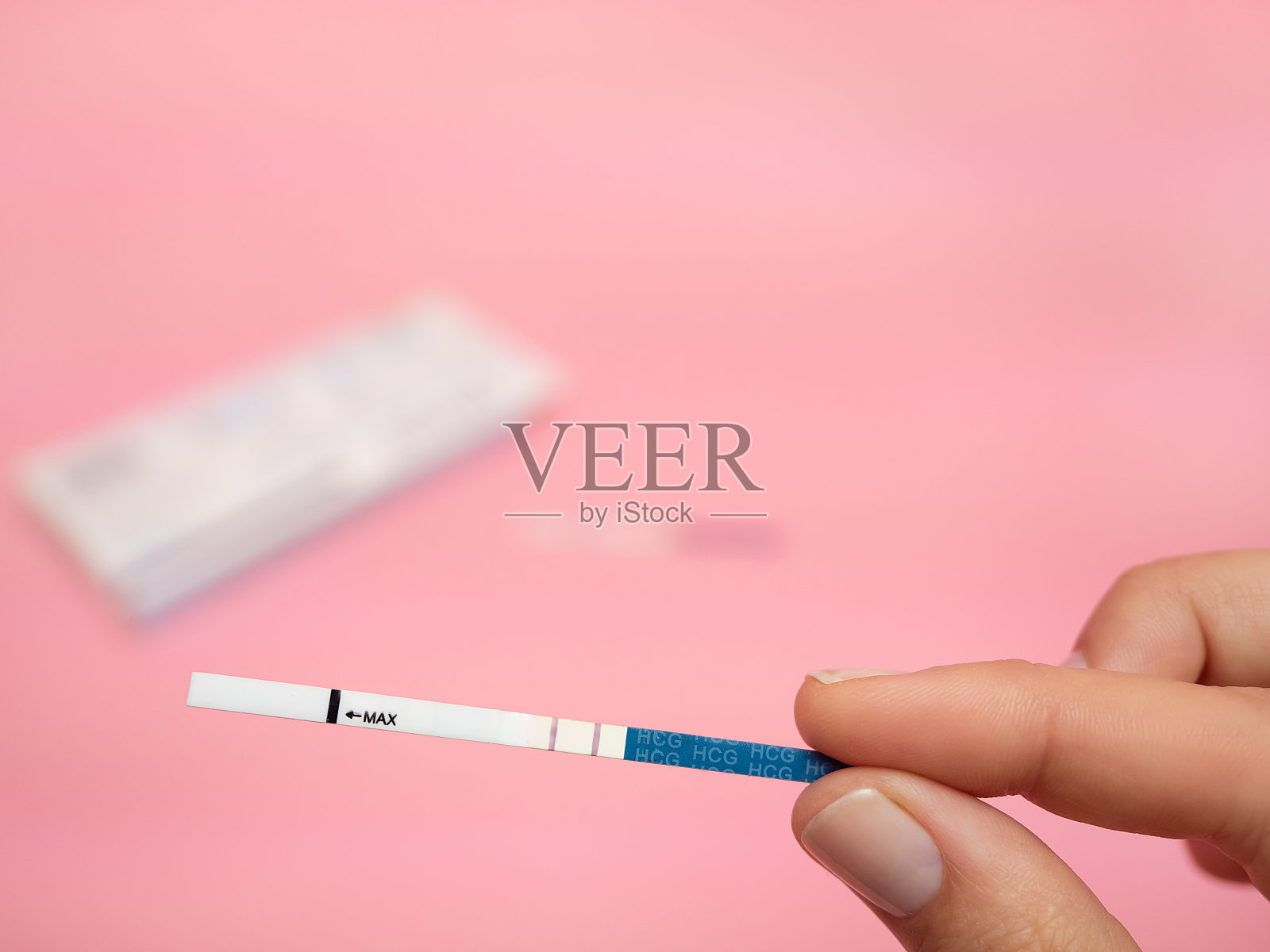 女性手握妊娠试验阳性，粉红色背景隔离。蓝条上的缩写HCG的意思是人绒毛膜促性腺激素是一种由围绕在生长中的胚胎合胞滋养层周围的细胞产生的激素照片摄影图片
