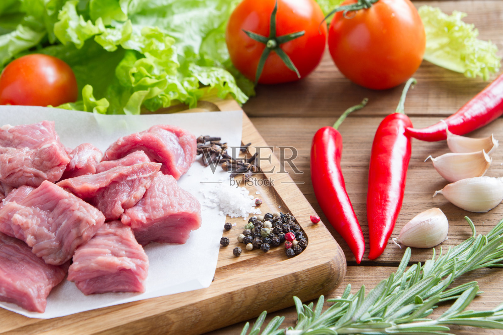 切成块的生牛肉。牛肉放在木板上。旁边是西红柿，辣椒，生菜，大蒜，辣椒，橄榄油。照片摄影图片