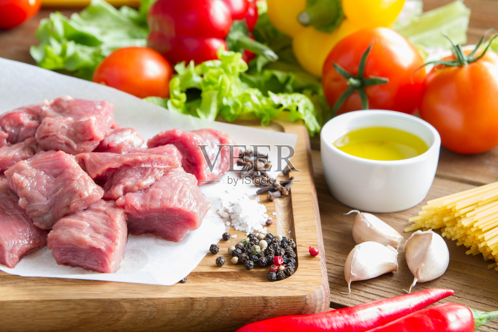 切成块的生牛肉。牛肉放在木板上。旁边是西红柿，辣椒，生菜，大蒜，辣椒，橄榄油。照片摄影图片